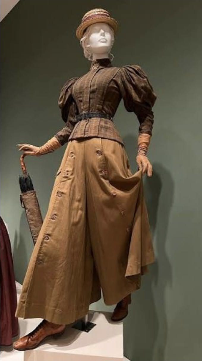 Mannequin wearing a brown 19th-century walking suit with a hat and umbrella.