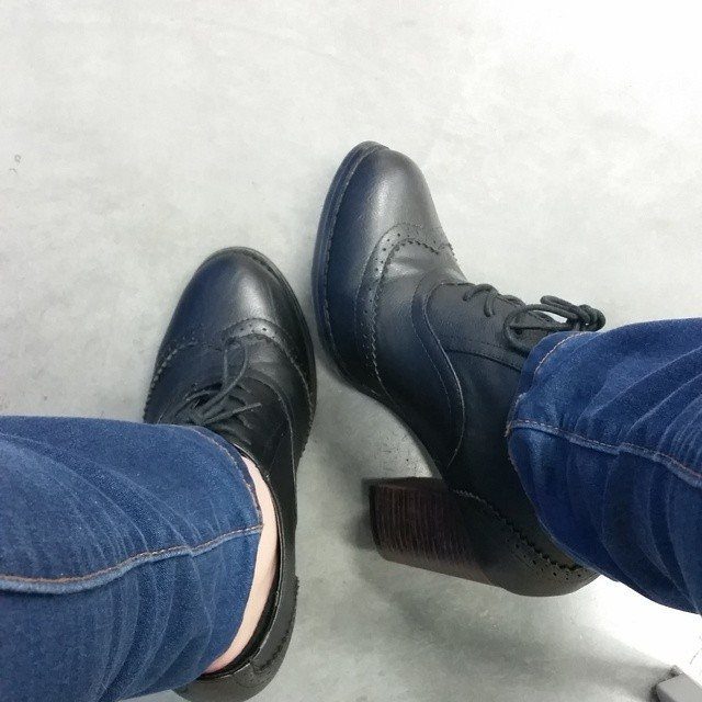 Black leather lace-up wingtip heels with chunky brown heels and blue jeans.