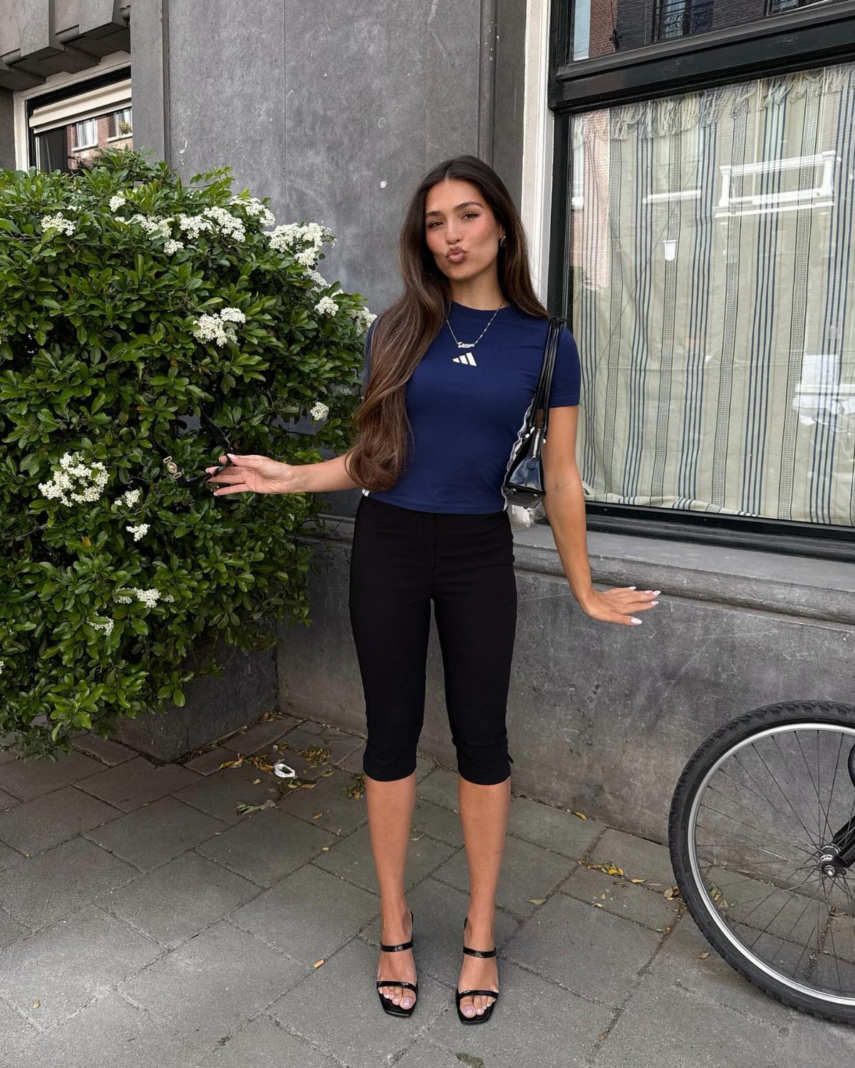Woman wearing a navy Adidas t-shirt and black capri pants posing on sidewalk