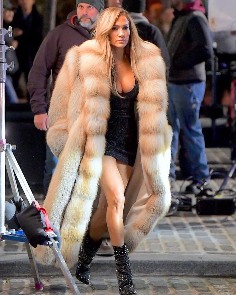 Woman wearing a long tan faux fur coat over a short black dress.