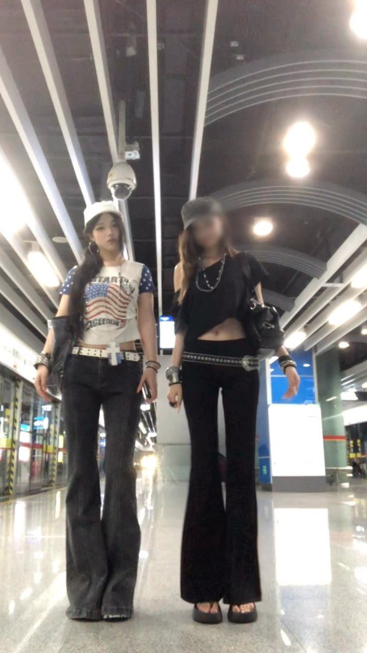 Two women wearing 2000s style flared pants and crop tops in a station.