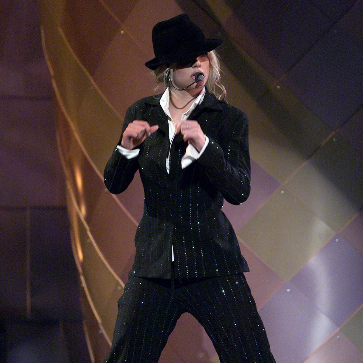 Woman in a sparkling black suit and hat performing on a stage.