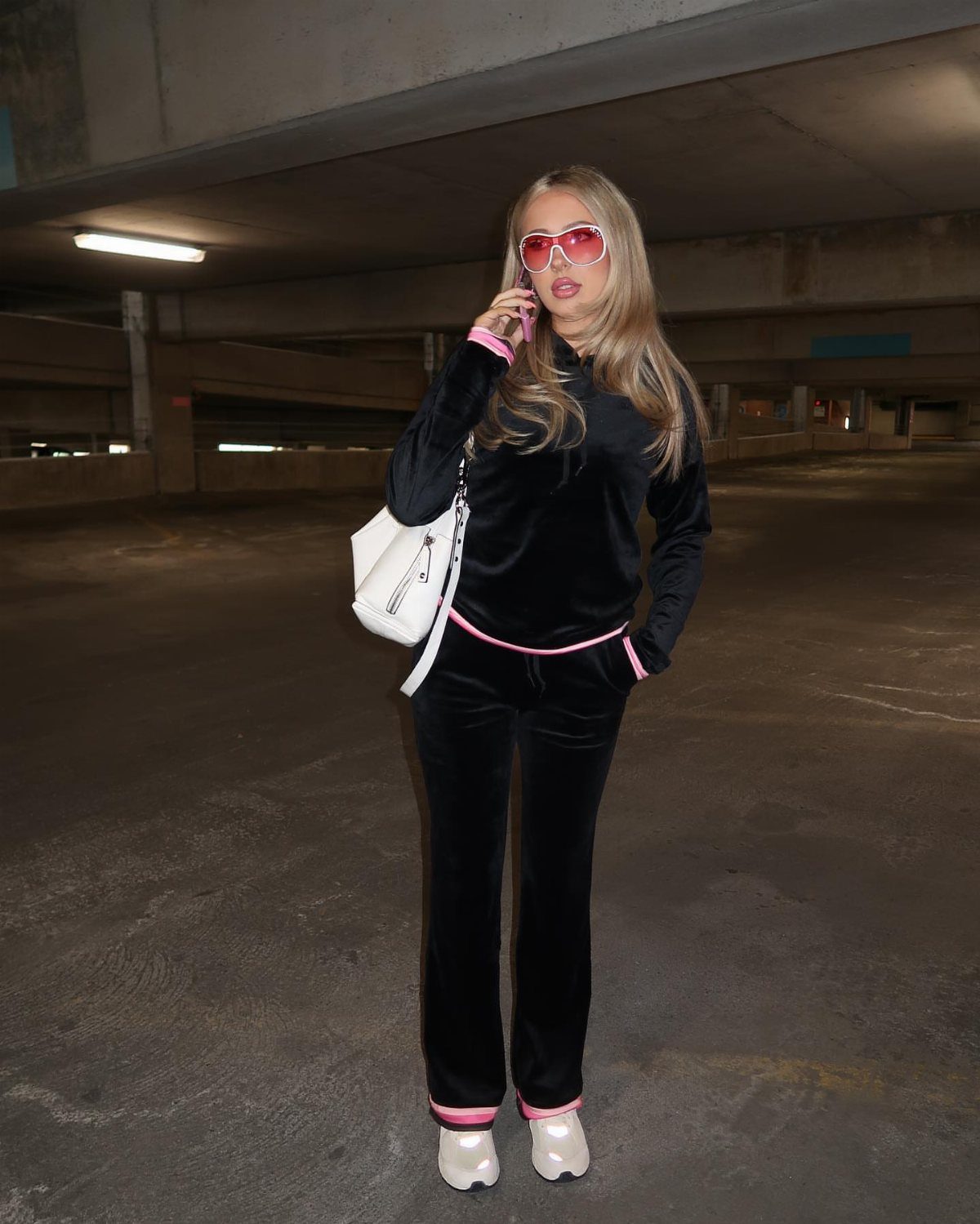 Woman in black velour tracksuit with pink trim standing in a parking garage.