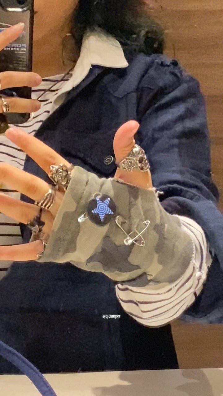 Camouflage fingerless glove with a safety pin and blue star on a hand.