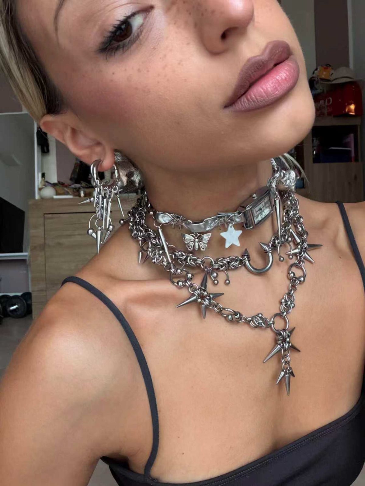 Person wearing multiple layered silver spiked necklaces and matching punk style earrings.