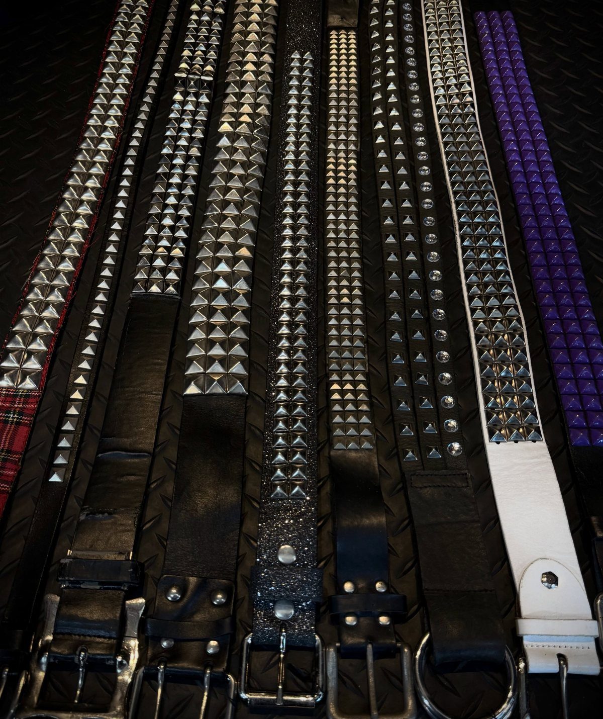 Various studded belts in black, white, and purple with silver metal pyramid studs.