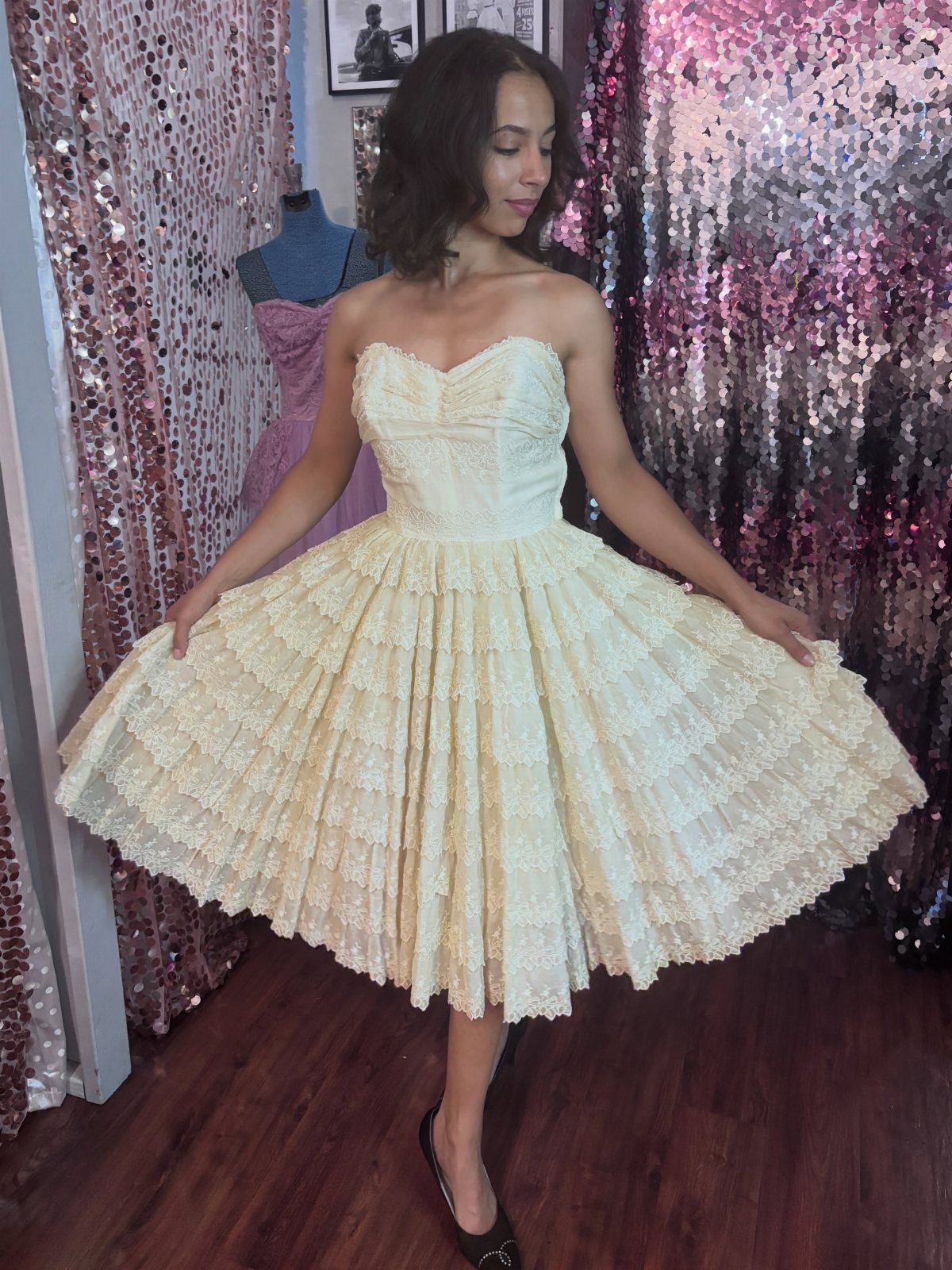 Woman wearing a strapless cream-colored 1950s style party dress with tiered lace skirt