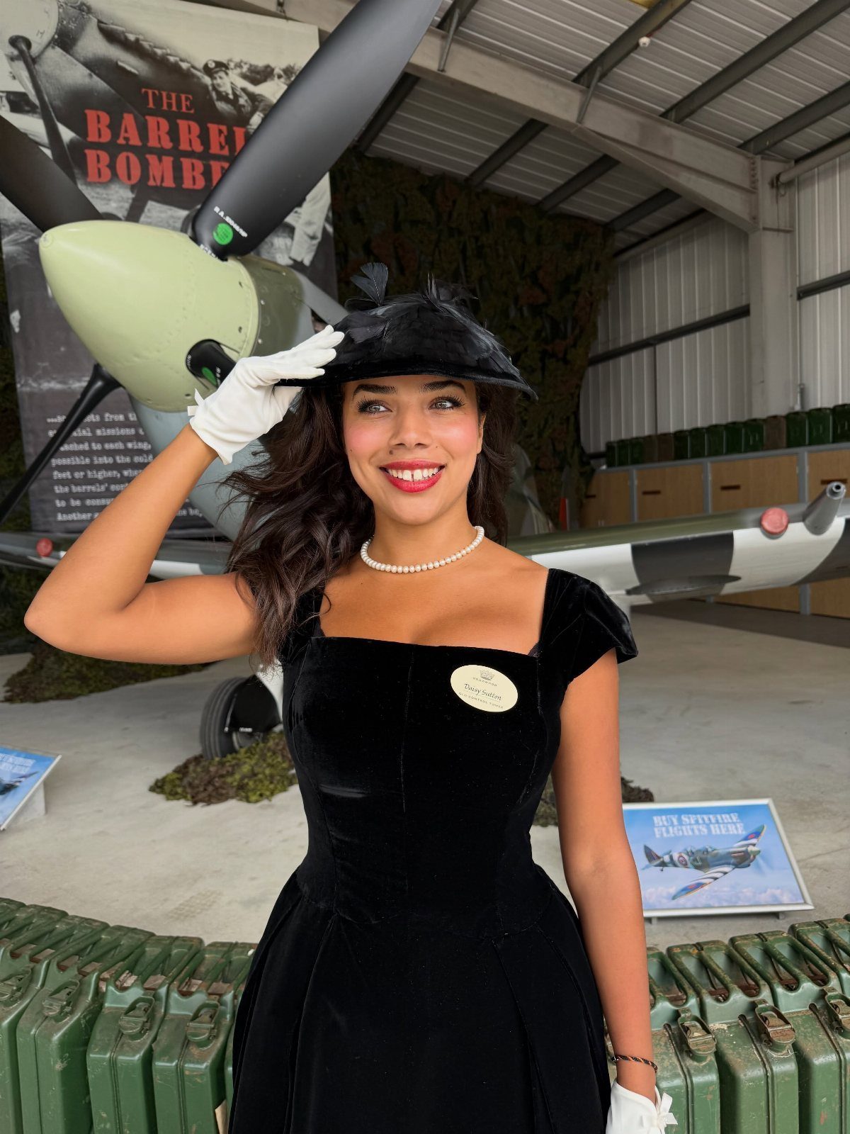 Woman in black velvet 1950s dress and hat posing by vintage aircraft