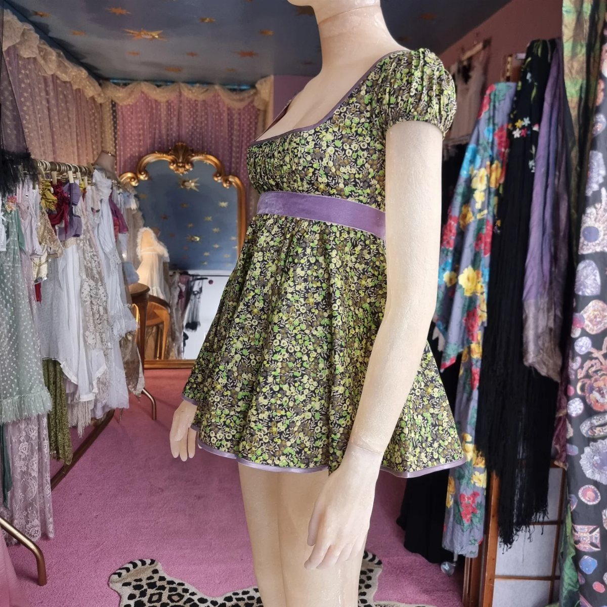 Green floral print vintage dress with purple waistband on a mannequin in a boutique