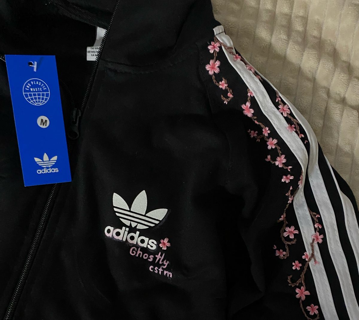 Black Adidas jacket with pink floral embroidery along the white sleeve stripes.
