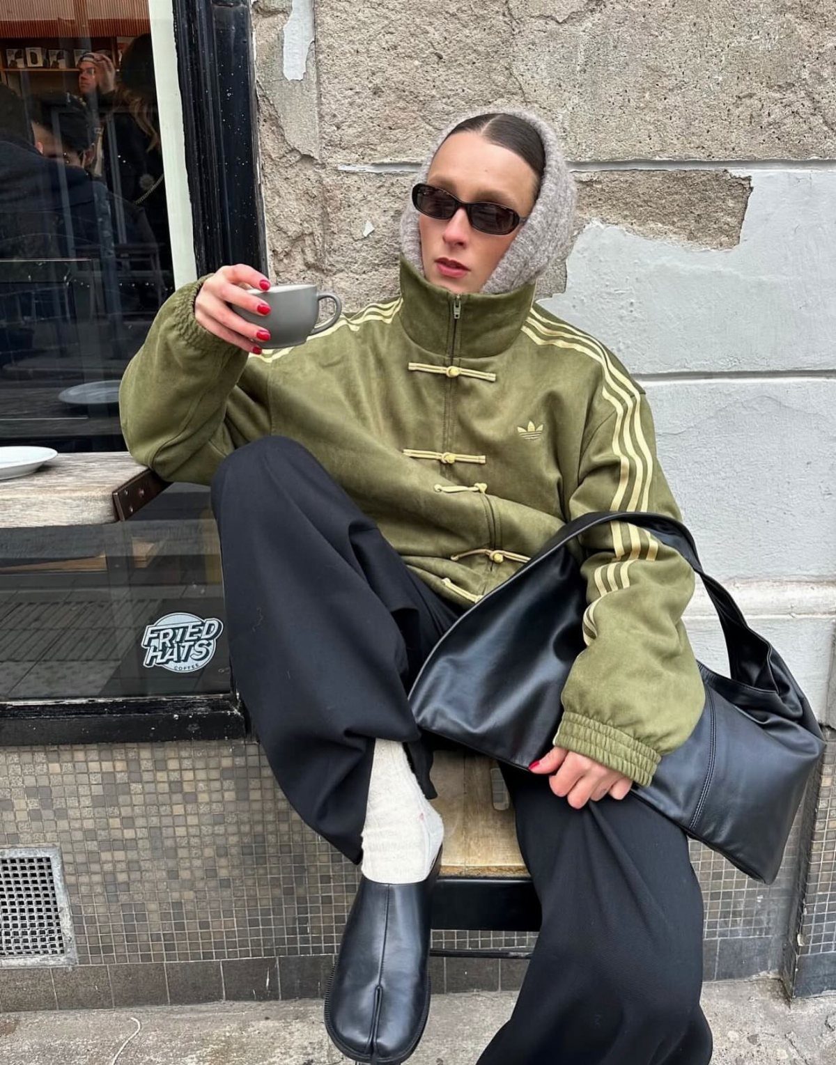 Person wearing olive green Adidas Chinese New Year jacket with frog fasteners sitting outdoors.