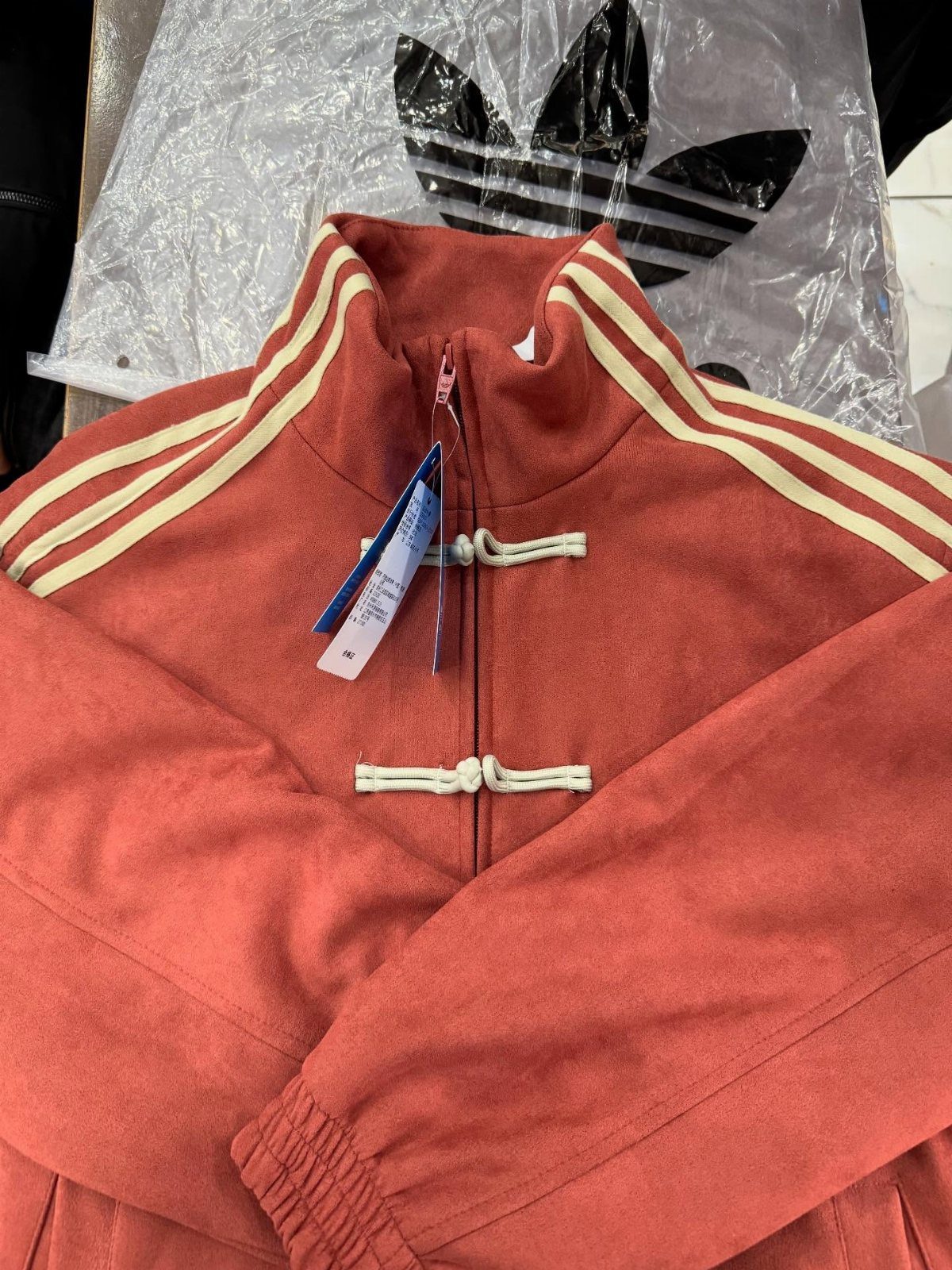 Red Adidas jacket with cream stripes and Chinese frog buttons on a flat surface