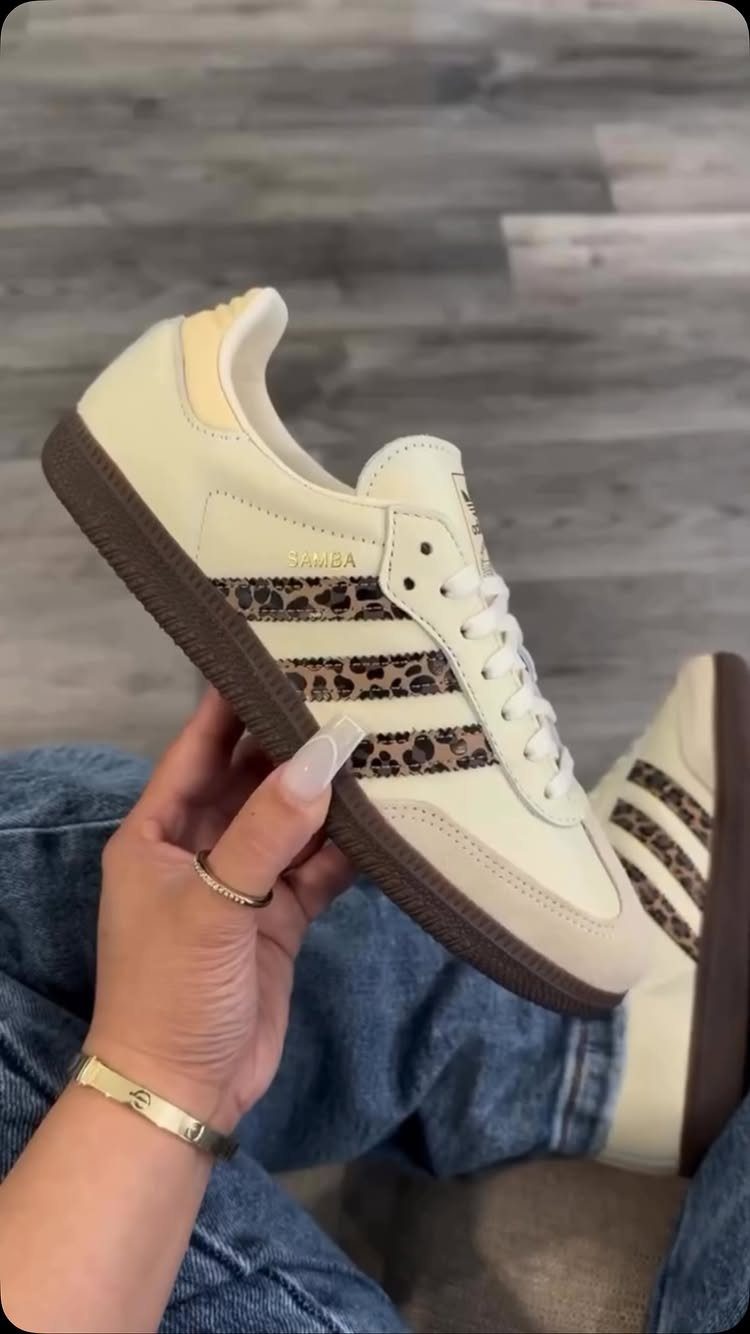 White Adidas sneakers with leopard print stripes held against blue denim jeans.