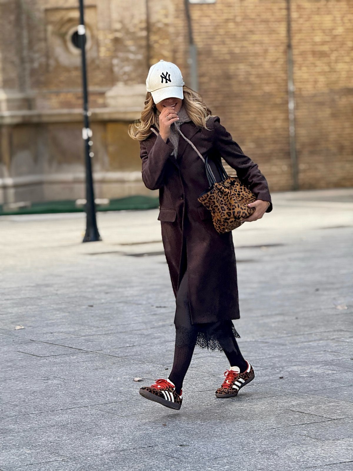 Person wearing leopard print sneakers, a dark brown coat, and a white cap.