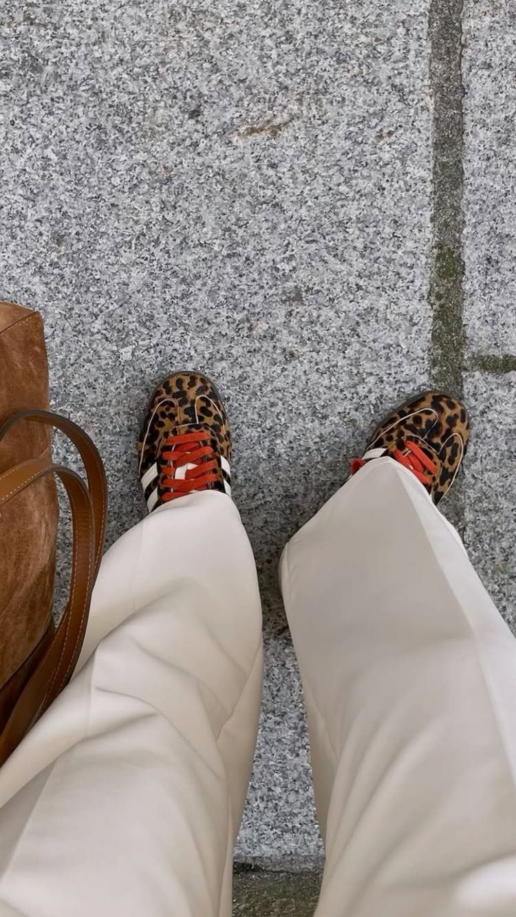 Leopard print sneakers with red laces and white trousers on grey stone ground.