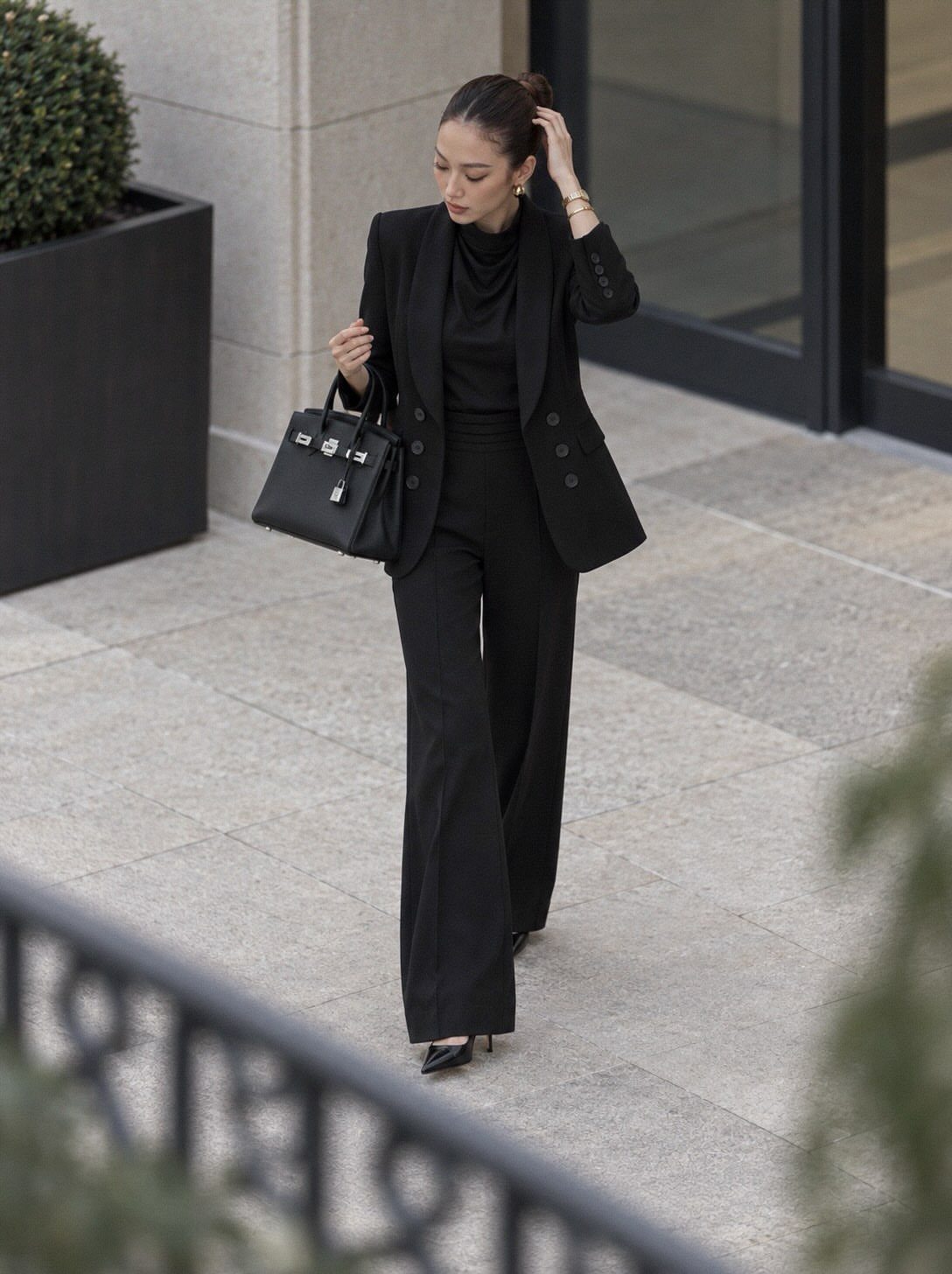 Woman in all black blazer and wide-leg trousers carrying a black leather handbag.