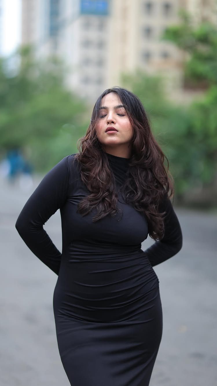 Woman wearing a long-sleeved black bodycon dress standing on a city street.