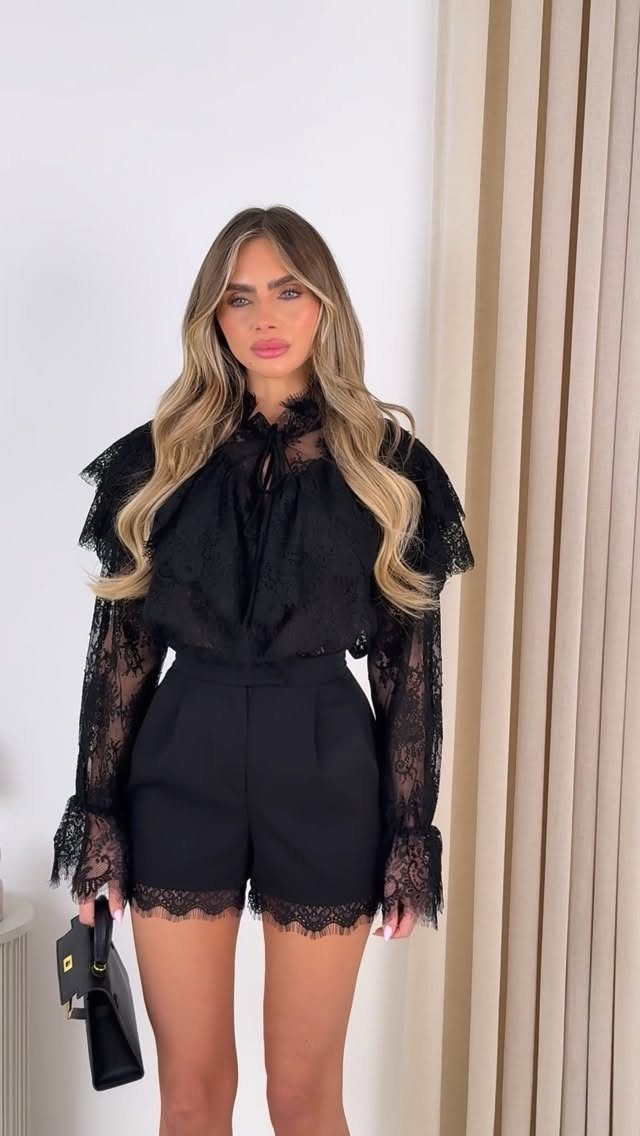 Woman in black lace long-sleeve blouse and matching lace-trimmed black shorts.