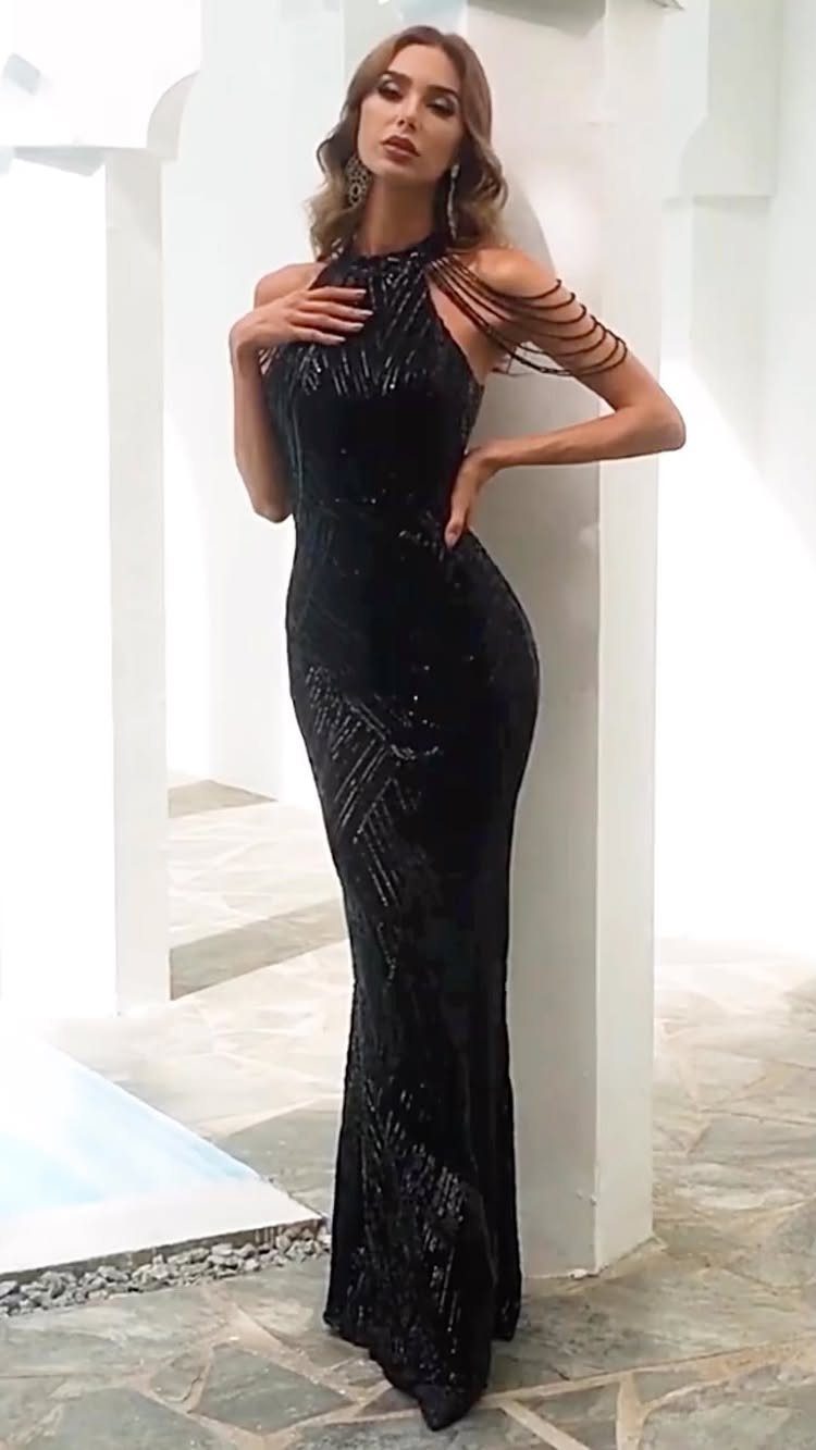 Woman wearing a floor-length black sequined gown posing against a white pillar.