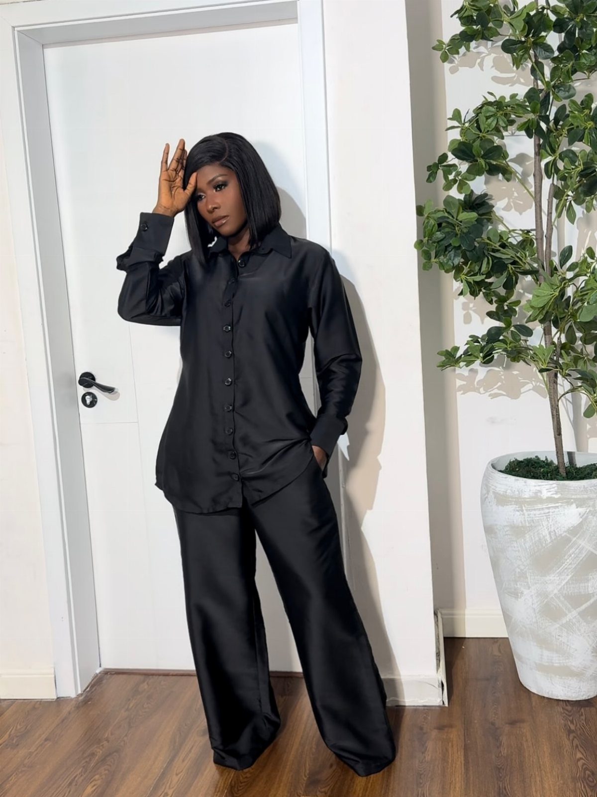 Woman wearing a black satin button-down shirt and matching wide-leg trousers indoors.