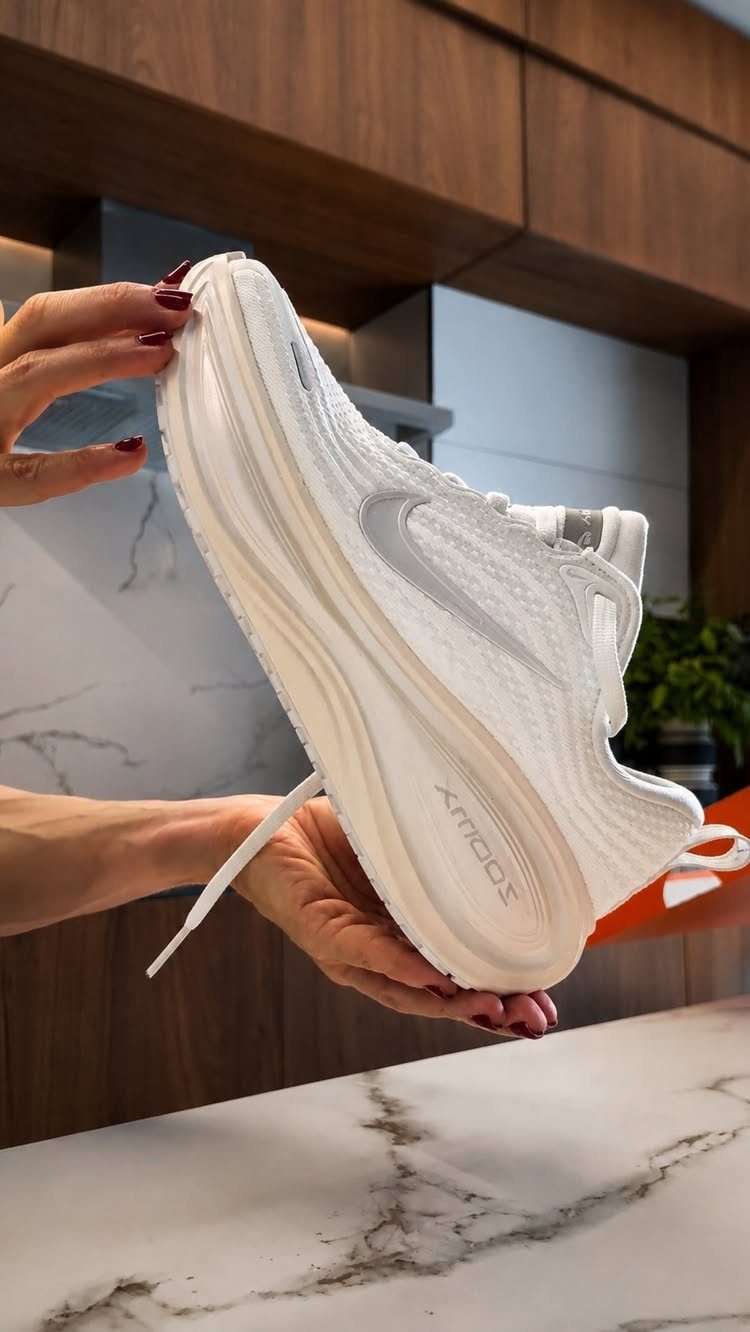 All-white Nike sneaker held by hands in a modern kitchen setting.