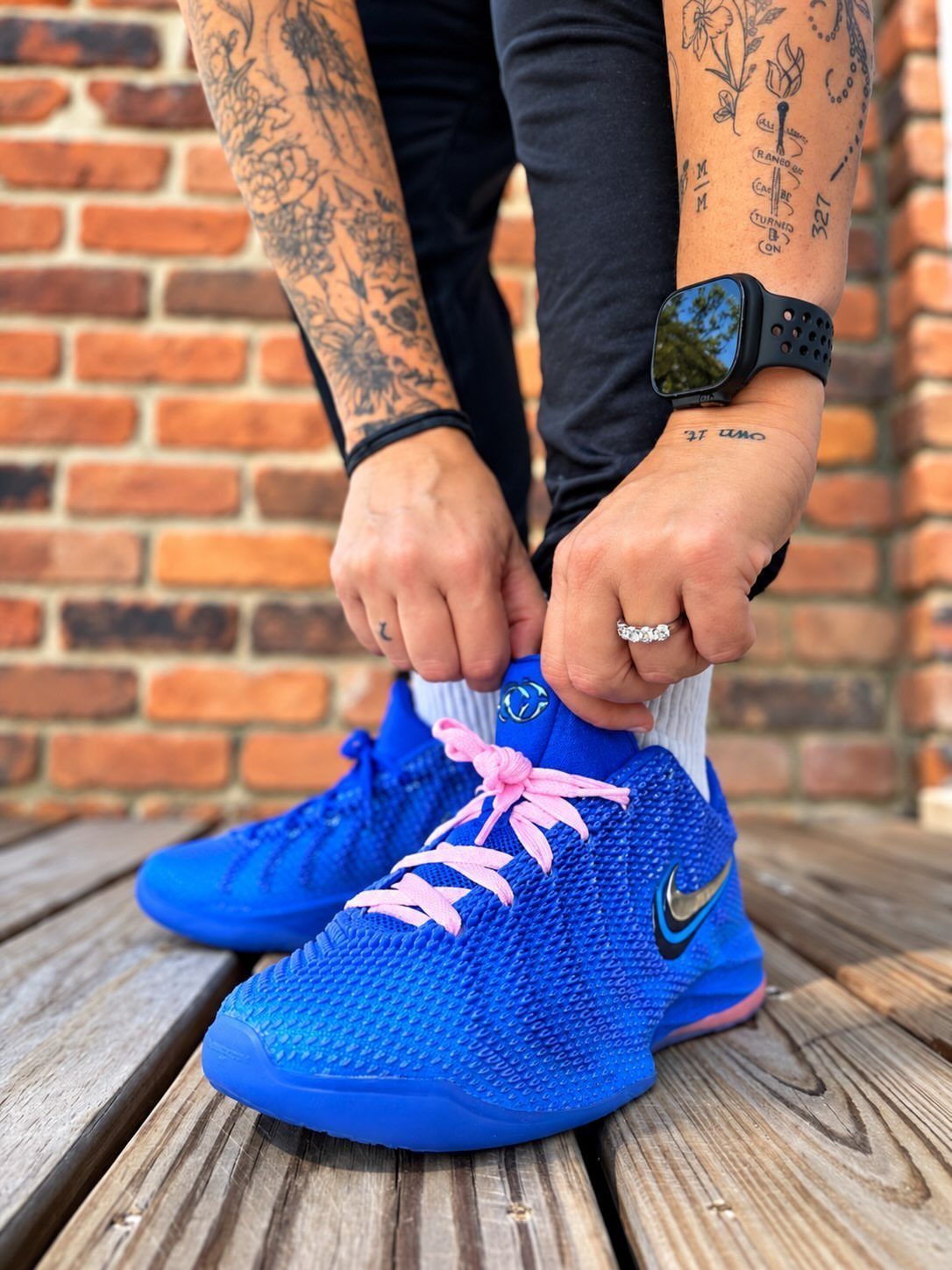 Blue Nike sneakers with pink laces being tied by a person on wood.