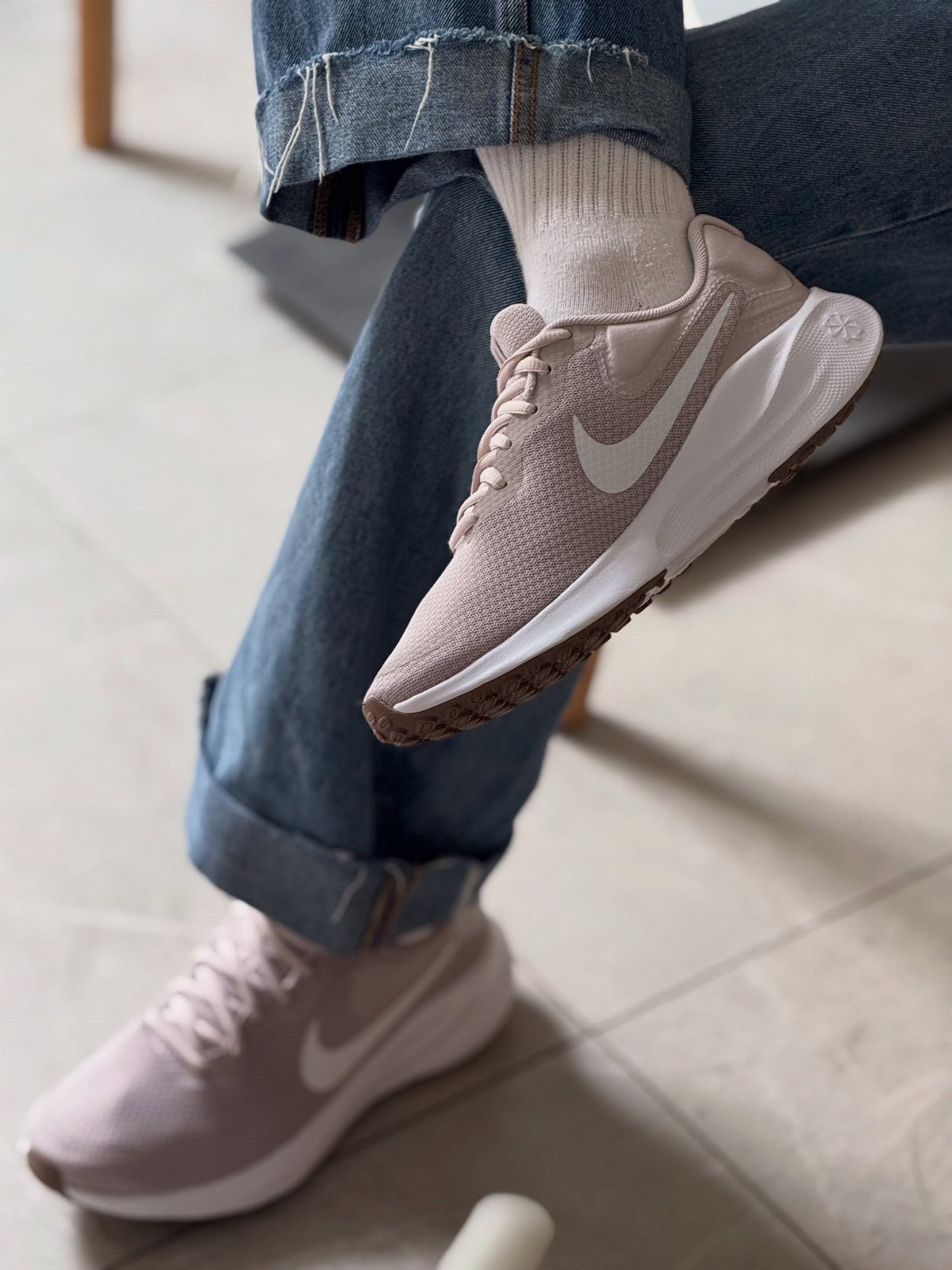 Light pink Nike sneakers with white swooshes worn with blue denim jeans.