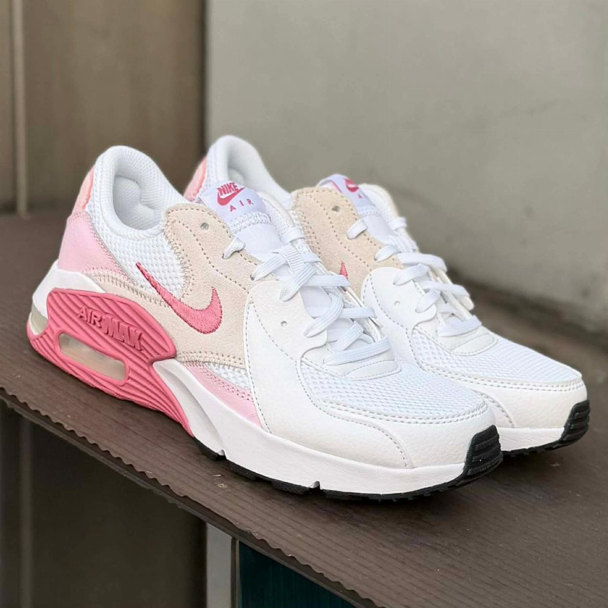 White and pink Nike Air Max sneakers with visible air cushioning on wooden ledge