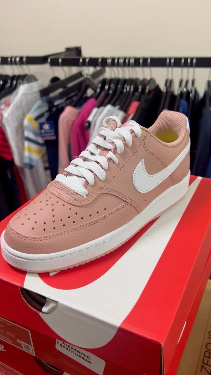 Pink Nike Court Vision sneaker with white swoosh resting on a red shoe box