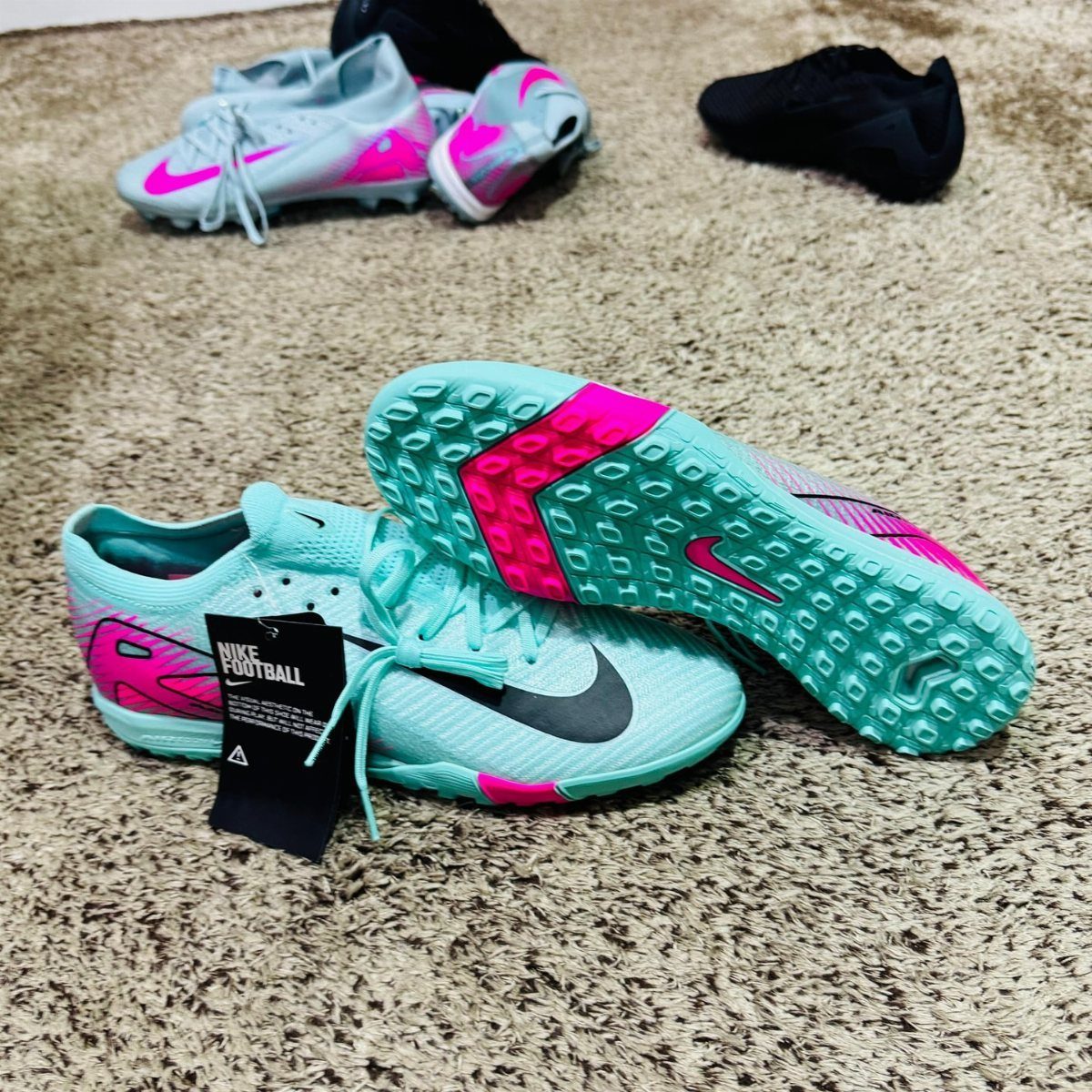 Light blue Nike football shoes with pink accents on a beige shag carpet
