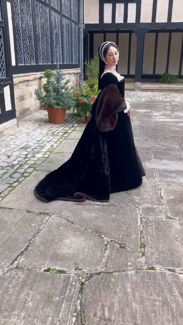 Woman in a black velvet Tudor gown and French hood standing in a courtyard