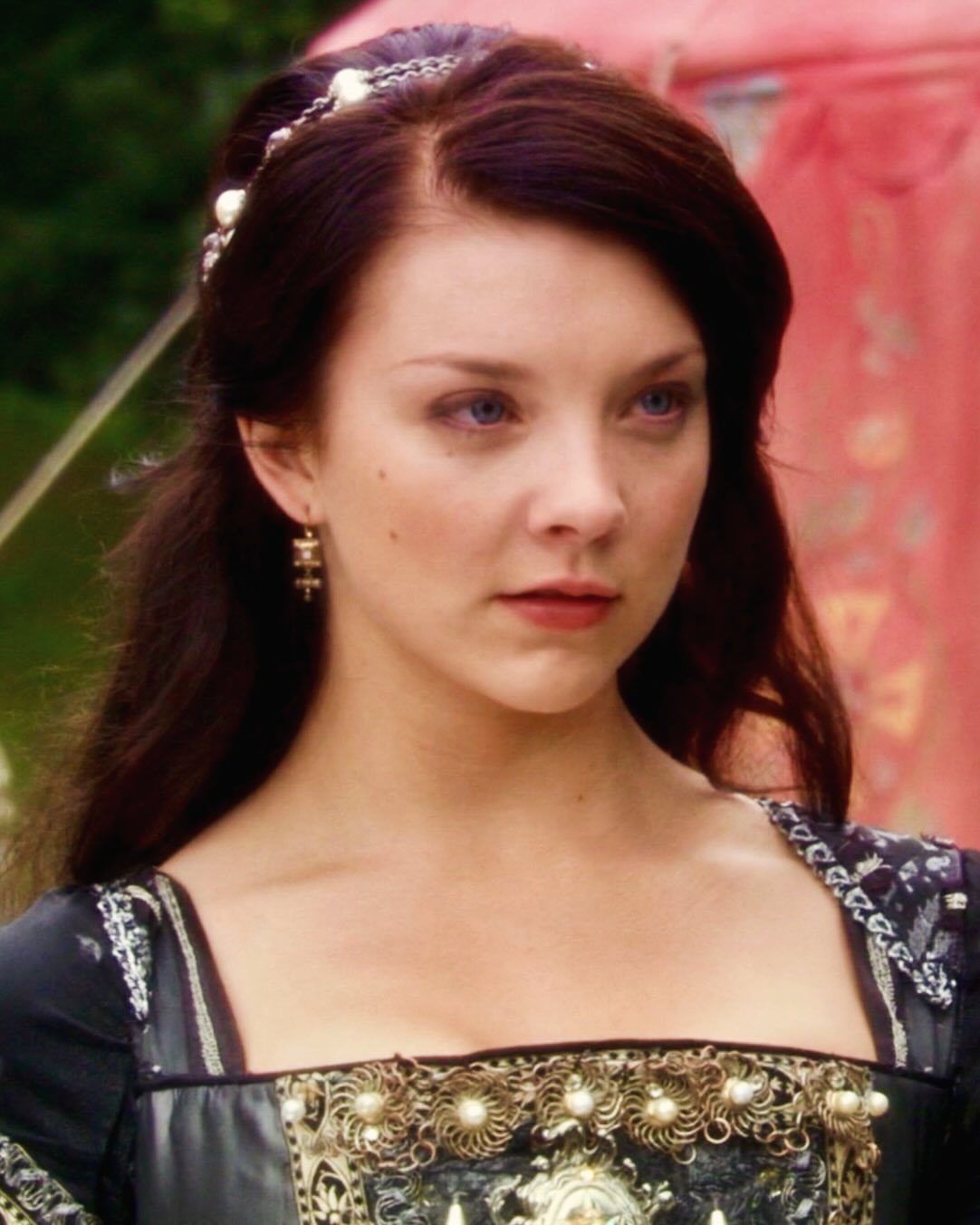 Woman in a black and gold Tudor gown with a pearl headband.