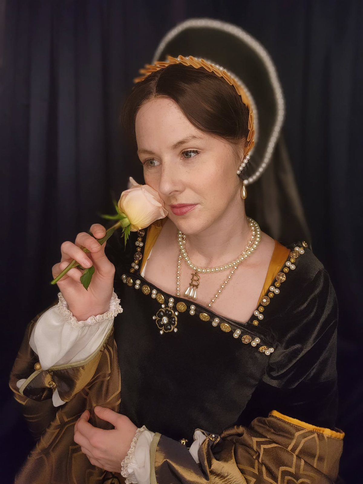 Woman in black velvet Tudor gown and French hood smelling a pink rose