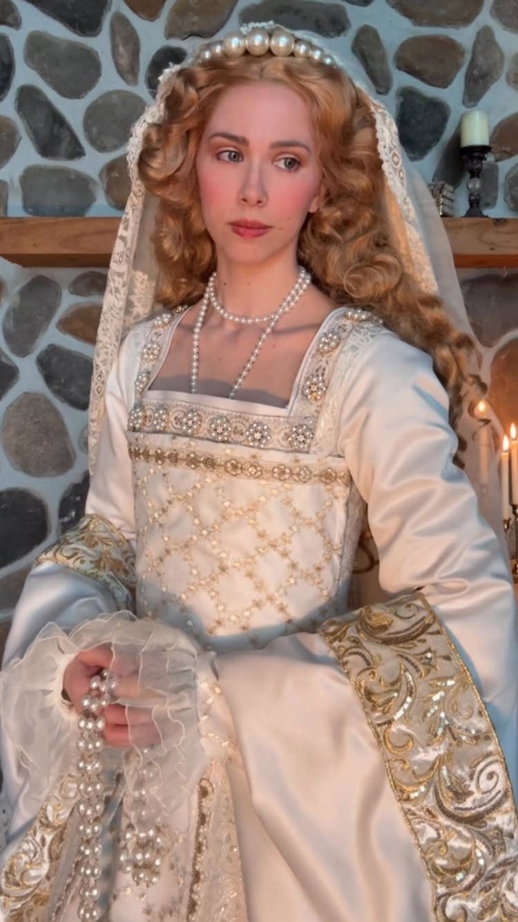 Woman in a white and gold Tudor gown with pearls and a veil.