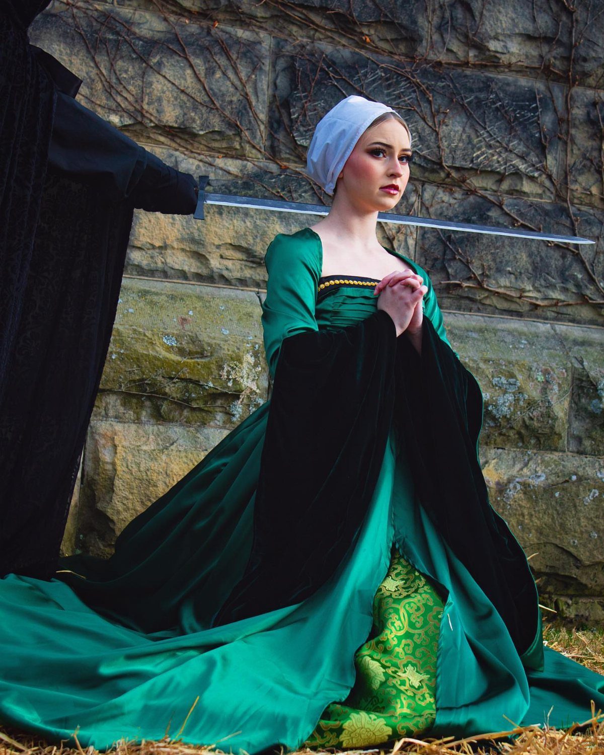 Woman in green Tudor gown and white cap kneeling before a sword