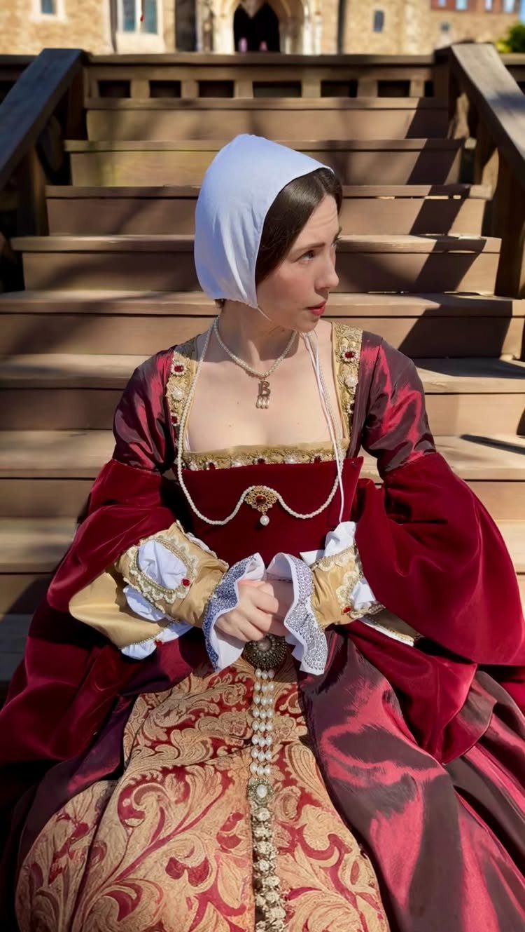 Woman in a red velvet Tudor gown and white gable hood sitting on stairs