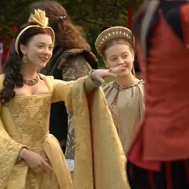 Woman in a yellow gold Tudor gown and French hood posing outdoors.