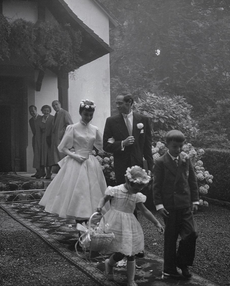 Woman in white wedding dress and rose crown walking with family outdoors.