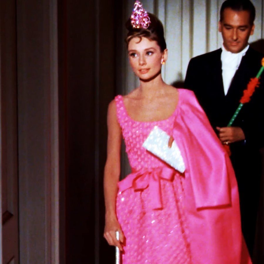 Audrey Hepburn in a sparkling pink gown, tiara, and cape with a tuxedoed man.