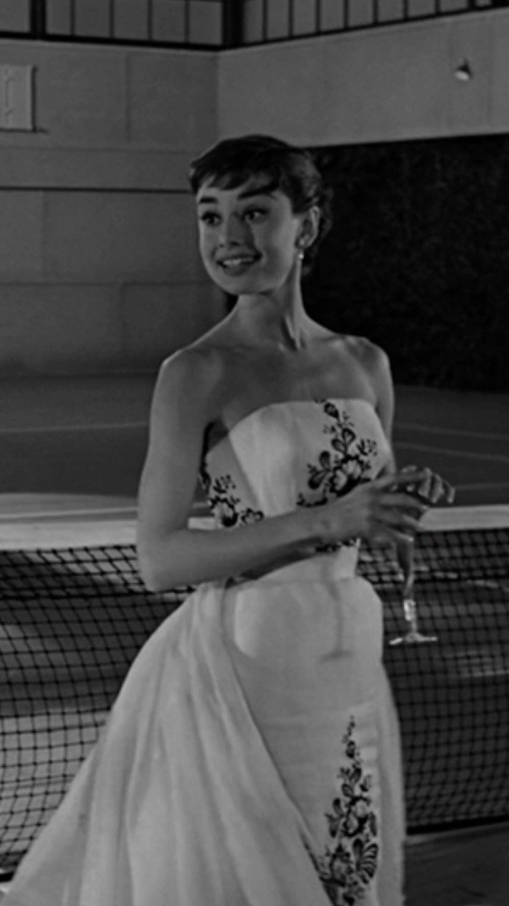 Audrey Hepburn in a strapless white floral gown holding a champagne glass.