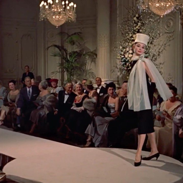 Audrey Hepburn wearing a black dress and white hat on a fashion runway