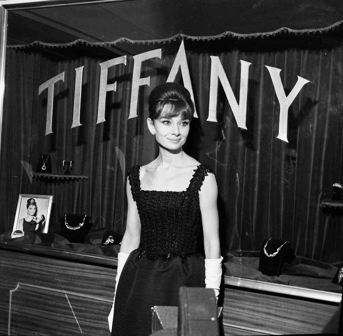 Audrey Hepburn in a sleeveless black sheath dress and white gloves before Tiffany's.
