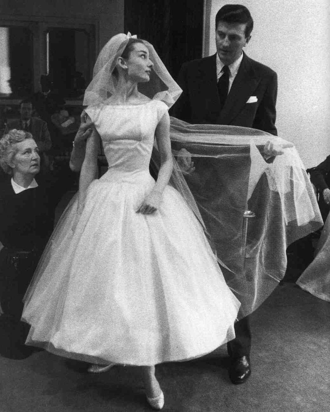 Audrey Hepburn wearing a white tea-length wedding dress and a short bridal veil.