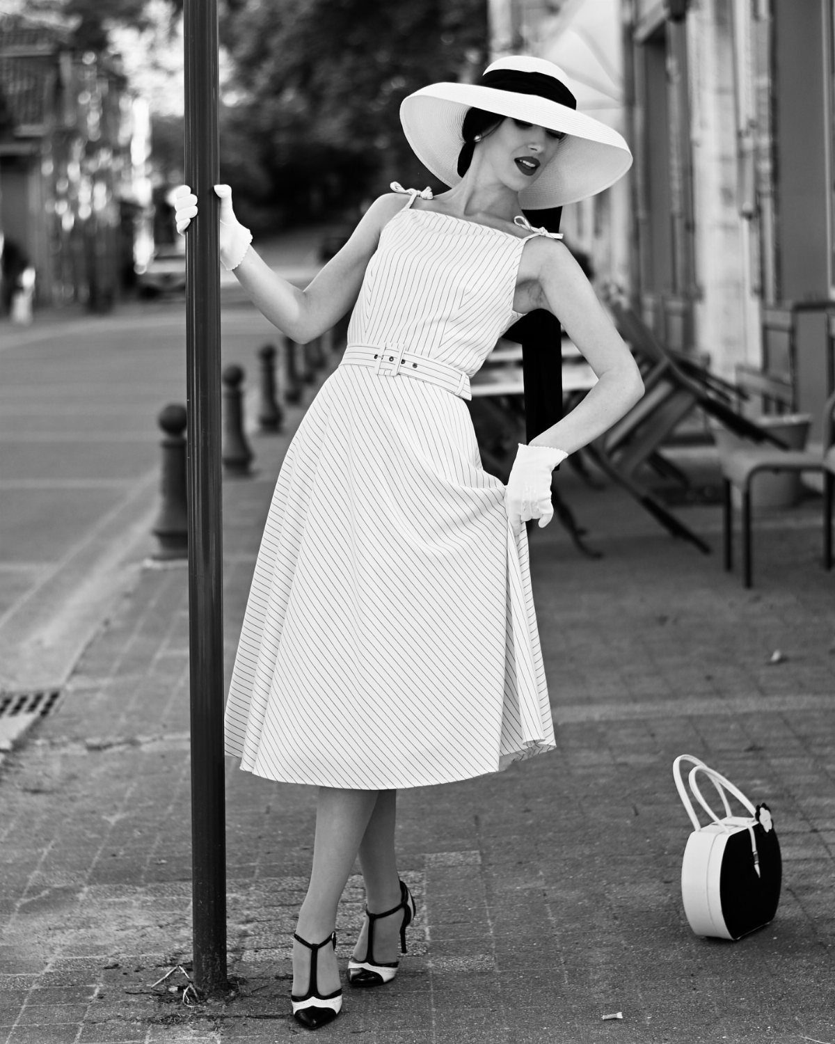 Woman in a vintage midi dress and wide-brimmed hat posing on a sidewalk