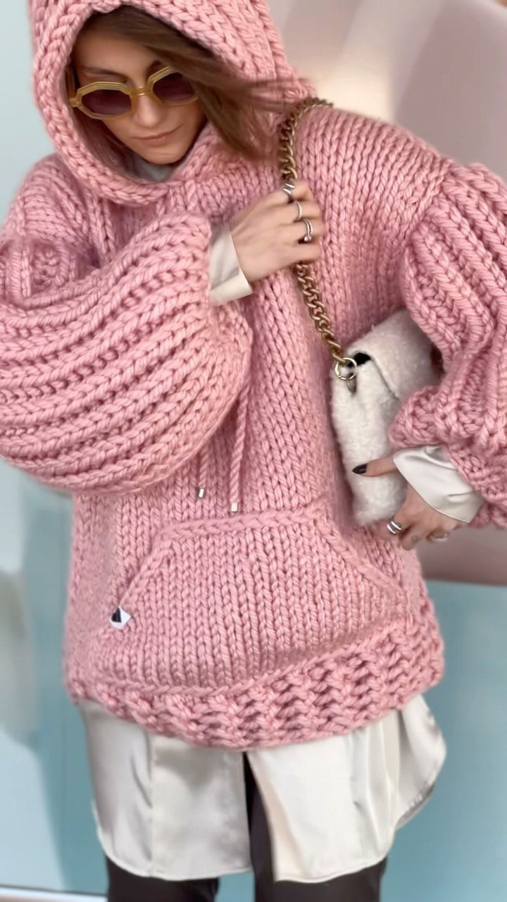 Woman wearing an oversized chunky pink knit hooded sweater and white fuzzy handbag.