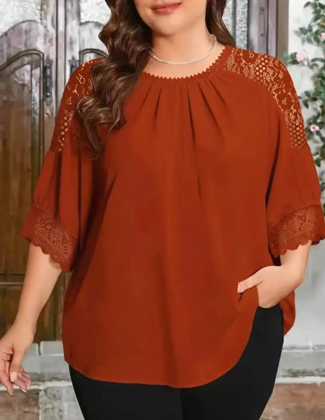 Rust-orange flowing blouse with lace details worn by a person with black trousers.