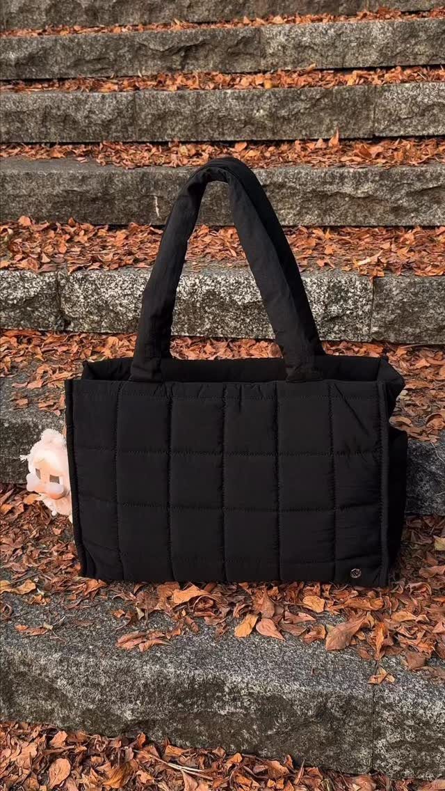 Black quilted puffer handbag resting on stone steps with autumn leaves.