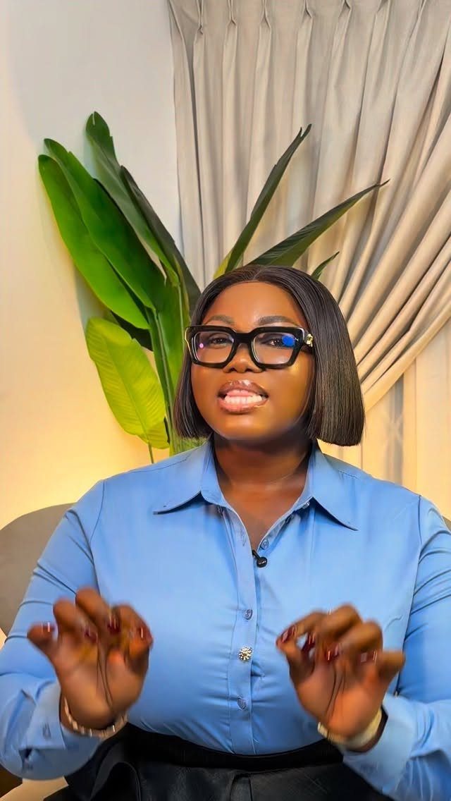 Woman wearing a professional blue button-down shirt and glasses in an office setting.