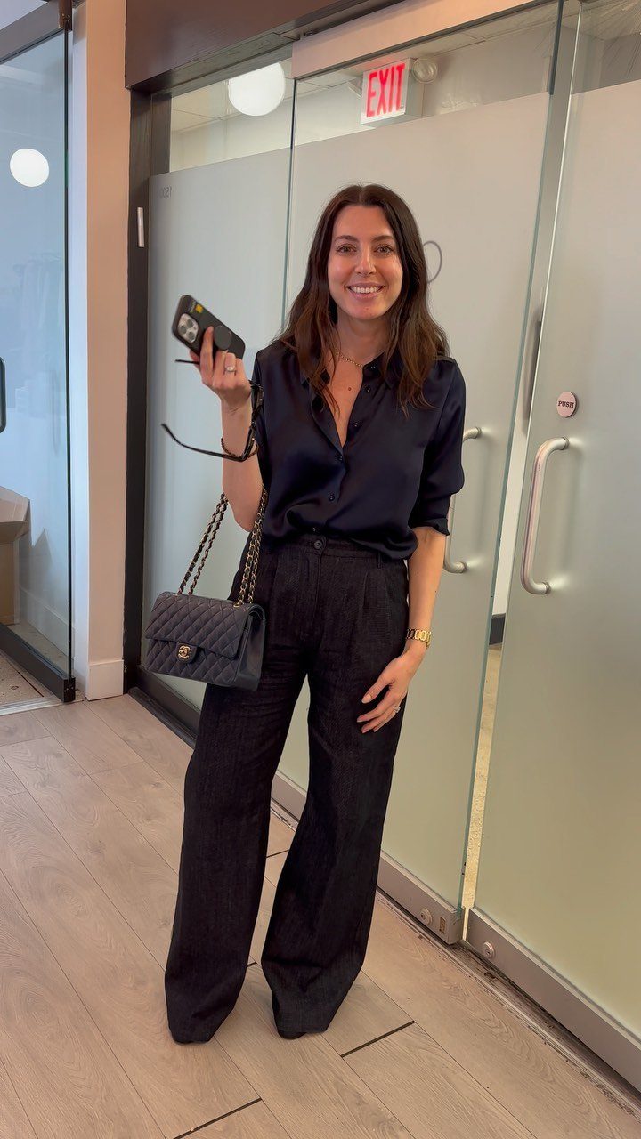 Woman wearing a navy blue blouse and black wide-leg trousers in an office.