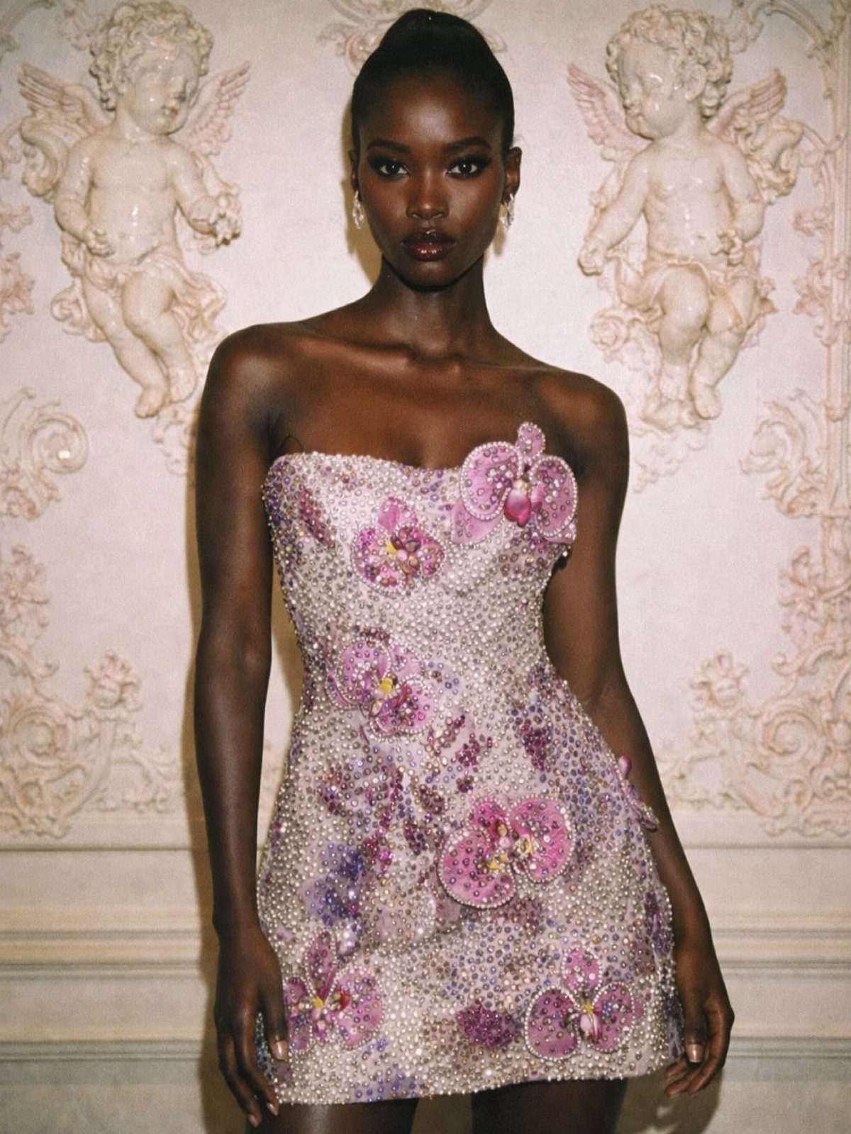 8 Beaded Formal Dress Ideas for Every Color and Style 4 Woman in a short pink beaded formal dress with floral details and cherub background
